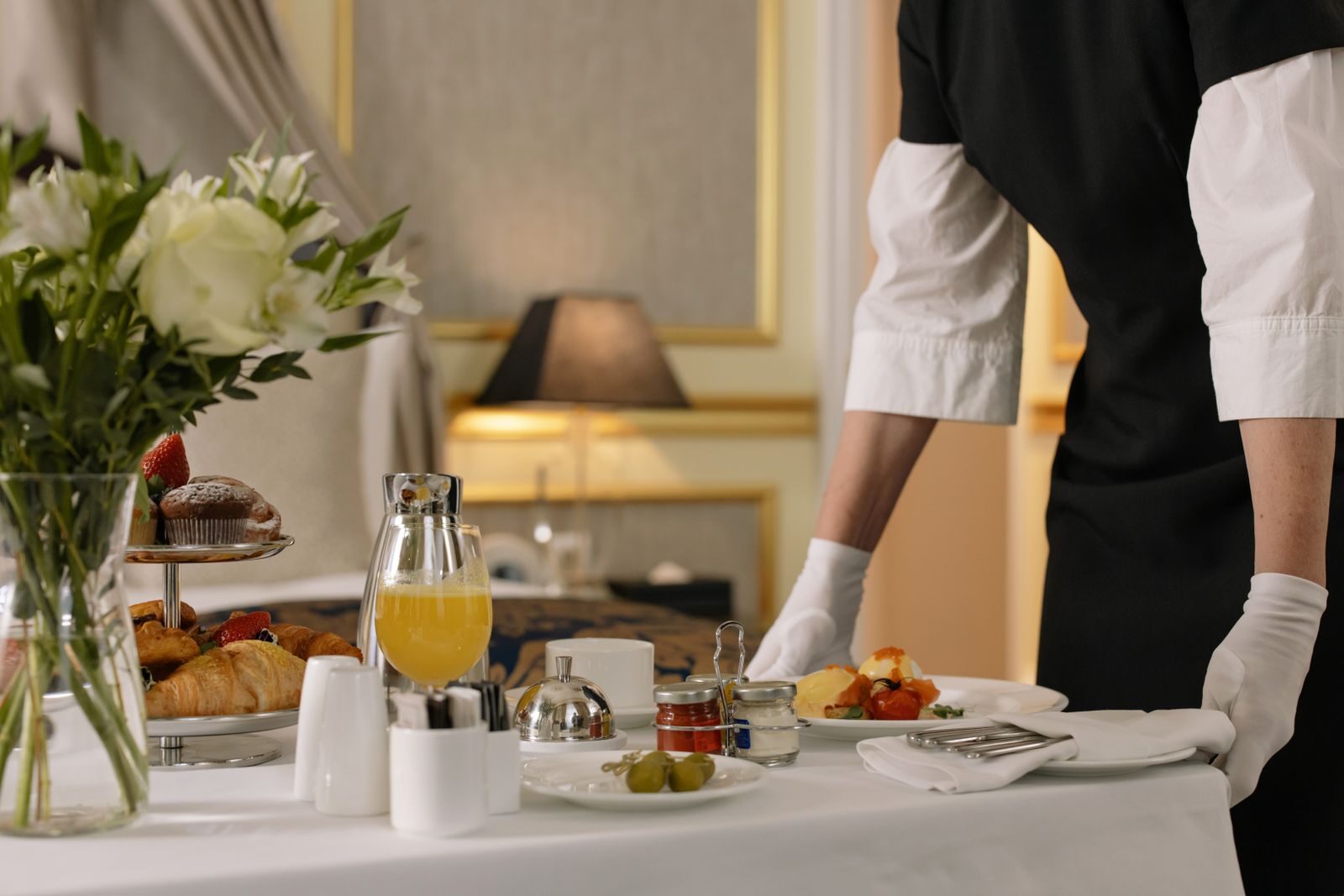 A luxurious hotel room showcasing an elegant room service breakfast setup with fresh flowers and a platter of assorted pastries.
