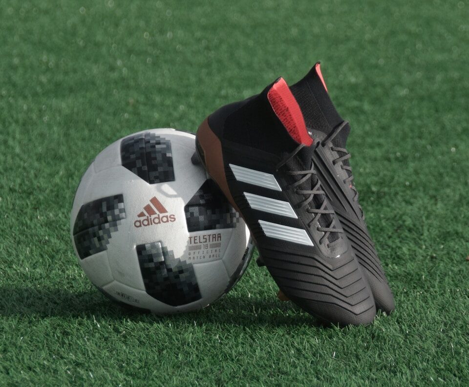 black adidas cleats lean on white and black adidas soccer ball on green grass